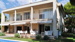 Ein modernes, zweistöckiges Haus mit Balkon, Pool und Sitzgelegenheit im Freien.