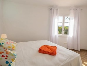A bedroom with a bed, a window with curtains, and a lamp.