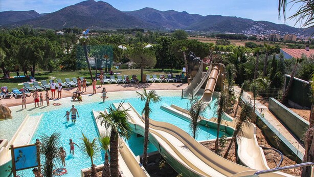 Un parc aquatique doté de nombreux toboggans et d’une piscine, entouré de palmiers et avec des montagnes en toile de fond.
