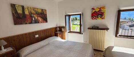 A bedroom with a bed, a nightstand, a window with a view of a garden, and a painting on the wall.