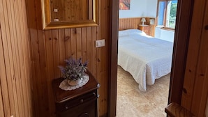 Een houten interieur met een spiegel, een klein tafeltje met een vaas en een bed met een witte deken.