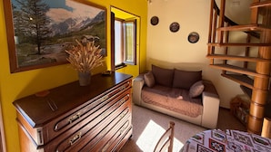 Een gezellige woonkamer met een houten dressoir, een bank, een schilderij van een berglandschap en een houten trap.