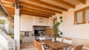An outdoor patio with a stone wall, a wooden table, and chairs.