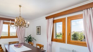 A dining room with a wooden table, chairs, a chandelier, and large windows with curtains.