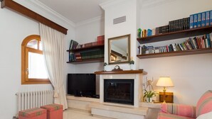 A living room with a fireplace, bookshelves, a television, and striped sofas.