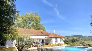 A villa with a swimming pool, surrounded by trees and a clear sky.