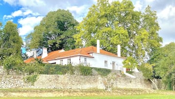 Situated in a lush, green environment, this traditional building features a red-tiled roof and a stone wall.