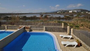Una piscina con dos sillas de descanso y vista a un paisaje costero con edificios al fondo.