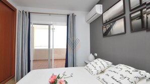 Un dormitorio con cama, ventana con cortinas, aire acondicionado y cuadros en la pared.