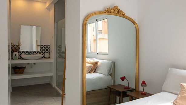 Une chambre avec un grand miroir, un lit, une table de chevet avec deux lampes et une vue sur un balcon.