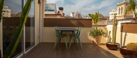 A rooftop terrace with a wooden deck, a table with two chairs, and potted cacti.