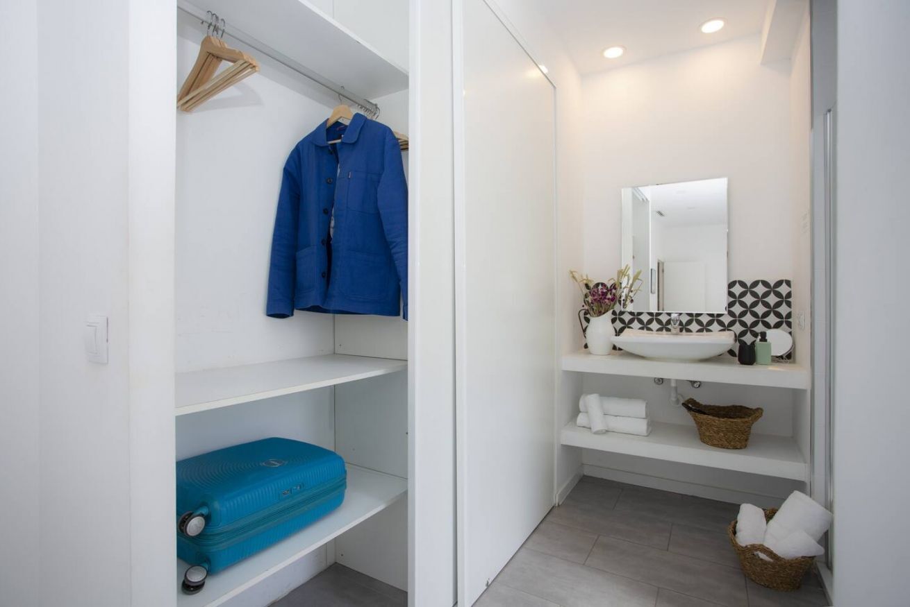 Une salle de bain avec un lavabo blanc, un miroir et des étagères contenant des articles de toilette.