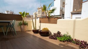 Une terrasse sur le toit, dotée d’un plancher en bois, de plantes en pot et d’une table avec des chaises.