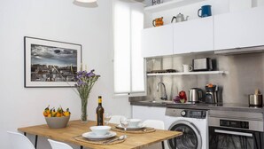 Une cuisine moderne avec des meubles blancs, une table à manger en bois et un lave-linge.