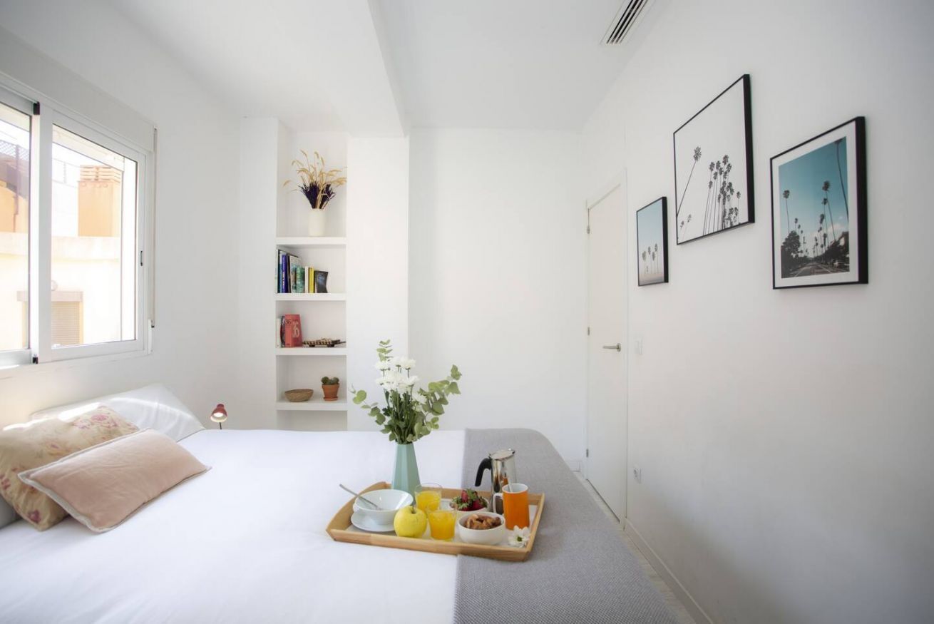 Um quarto com uma cama, uma mesa de cabeceira com uma bandeja de itens de café da manhã, uma estante e quadros nas paredes.