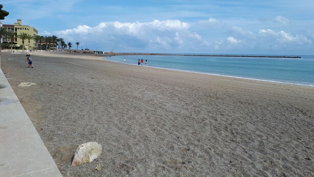 Ein weiter Sandstrand mit einem Hotel im Hintergrund und einem klaren Himmel.