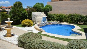 Ein Pool mit Felsen, umgeben von gepflegten Rasenflächen und verschiedenen Sträuchern.