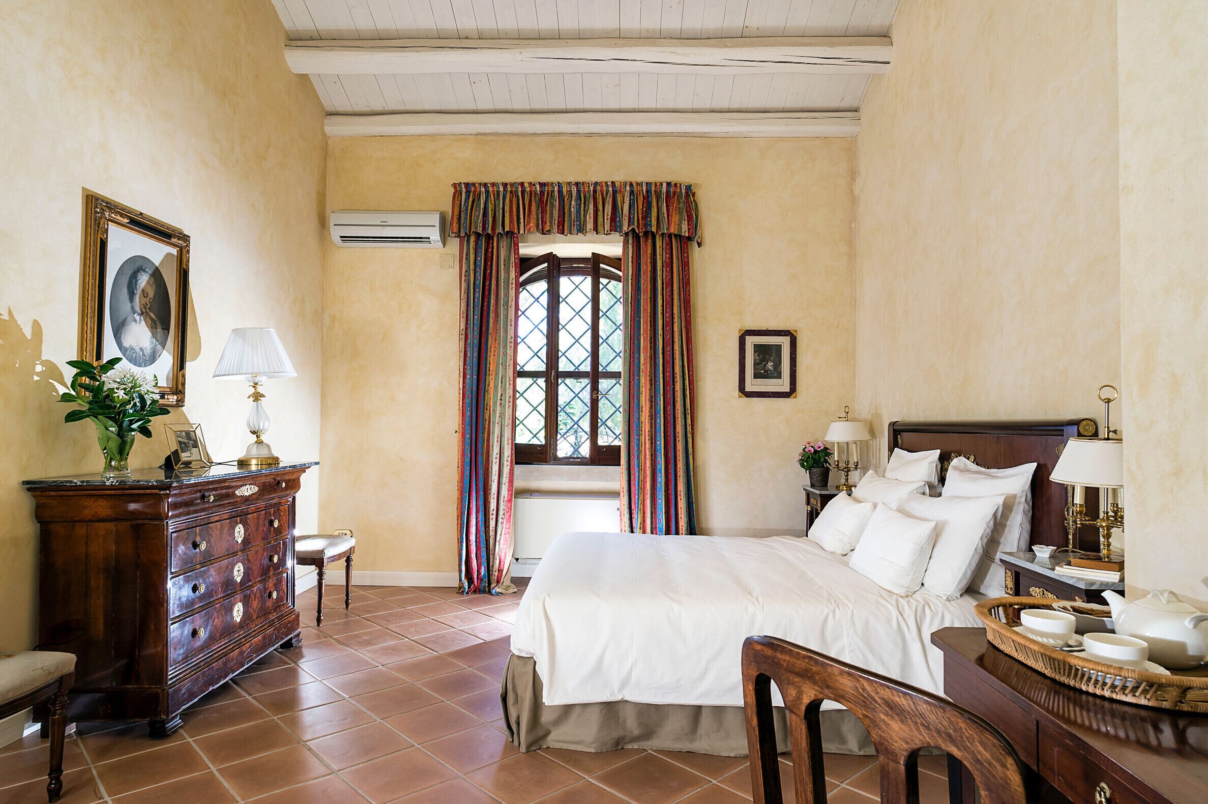 A bedroom with a bed, dresser, chair, and a window with curtains.