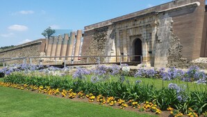 A historic building with a stone facade and an arched entrance, surrounded by a well-maintained garden with yellow and purple flowers. - Nice apartment in front of the sea in Roses Inmosantos Oasis E2 (Rosas / Roses)