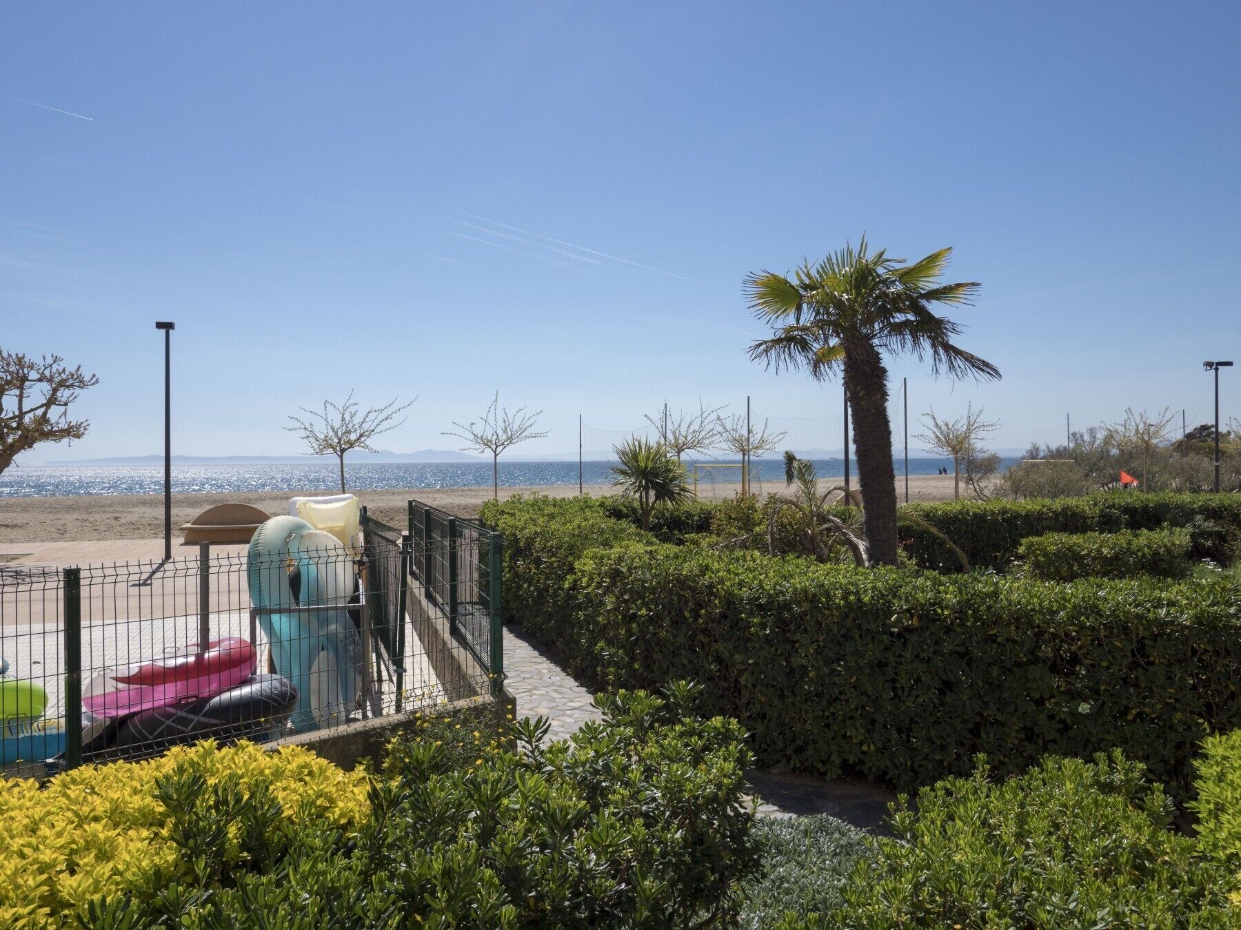 Un espacio exterior cercado con un parque infantil, palmeras y vistas a la playa y el océano.