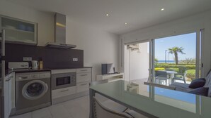A modern kitchen with a washing machine, oven, and microwave. There is a dining area with a table and chairs, and a view of the sea through large windows. - Nice apartment in front of the sea in Roses Inmosantos Oasis E2 (Rosas / Roses)