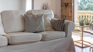 Ein helles Sofa mit vielen Kissen in einem gut beleuchteten Raum mit Holzboden und Blick auf Grünflächen.
