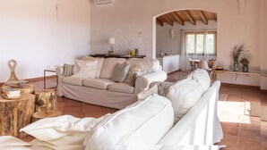 Ein geräumiges Wohnzimmer mit einer großen beigen Couch, Holzbalken an der Decke und einem durch einen Bogen sichtbaren Küchenbereich.