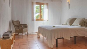 Ein Schlafzimmer mit Bett, Stuhl, Fenster und einem kleinen Regal mit Handtüchern.