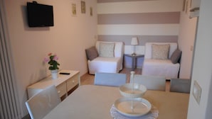 Una habitación moderna y bien iluminada con una mesa de comedor, dos sofás, un televisor y una pequeña mesita.