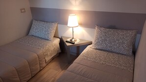 Dos camas individuales con ropa de cama estampada, una mesita de noche con lámpara e interruptor de luz en la pared.