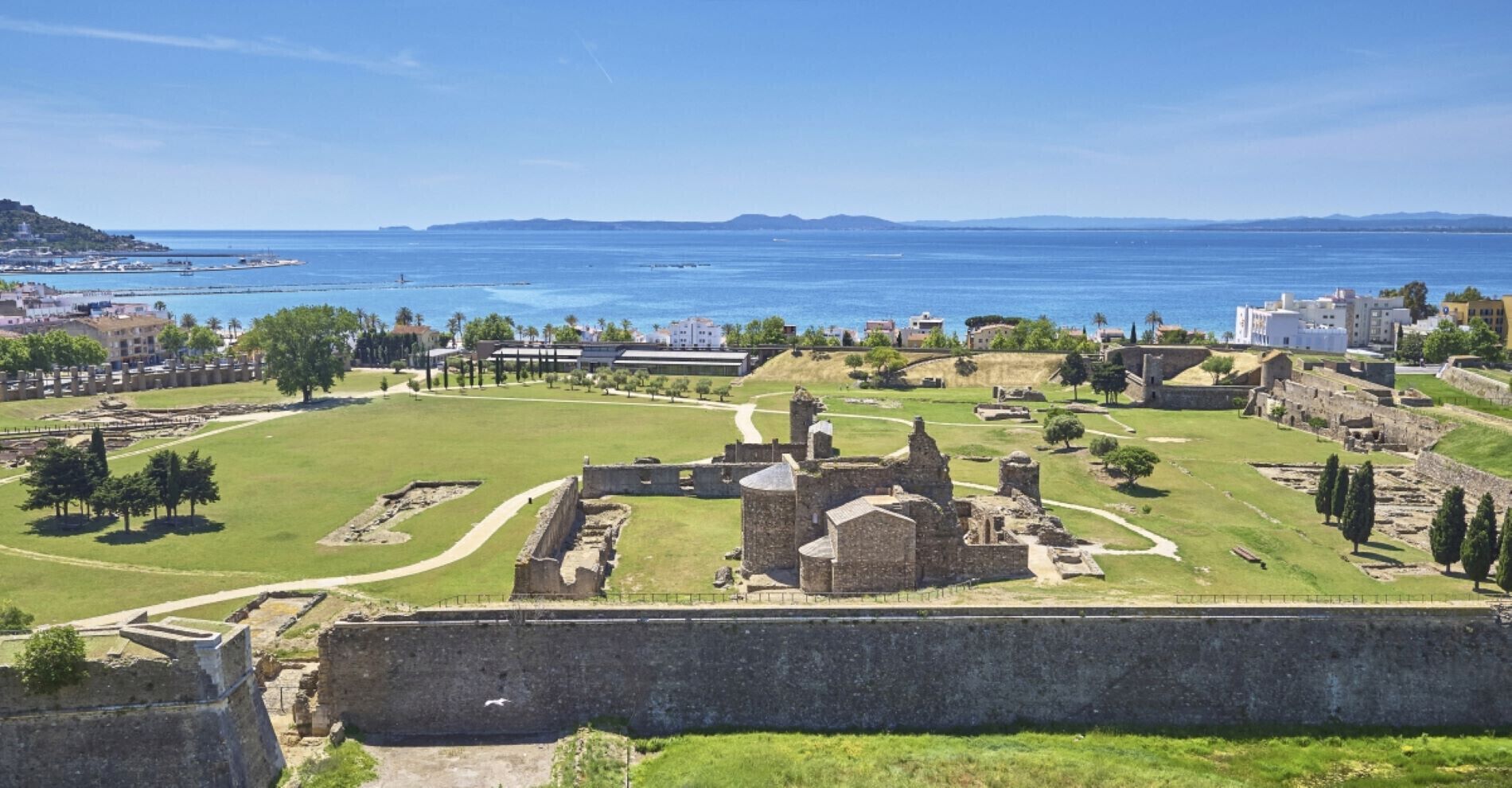 A historical site with ruins, a large open grassy area, and a view of the sea.