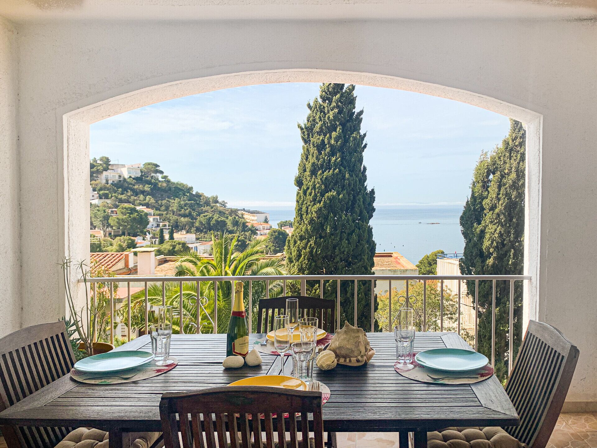 A dining table set for four with a view of the sea and hills.
