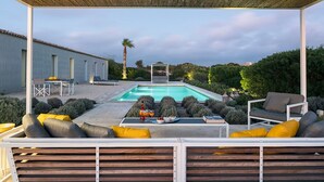 A poolside area with a covered seating area, a table with food and drinks, and a view of the pool and surrounding greenery. - Designer country villa with pool in Ragusa, Sicily (Ragusa)
