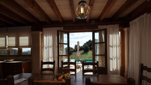 A dining area with a wooden table and chairs, a fruit bowl, and a view of a pool and greenery outside. - Son Horlandis, Country house in Petra, Mallorca (Petra)