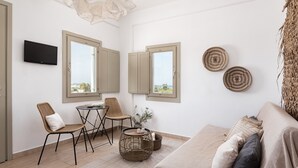 A modern living room with a sofa, two wicker chairs, a small table, and a TV mounted on the wall. - PAROS HOUSE - Ground Floor of a Villa for 6 persons Private Pool and Sea View (PAROS)