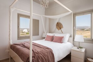 Un dormitorio con cama con dosel, una mesita de noche con lámpara y vistas al paisaje por las ventanas.