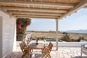 Un espacio de estar al aire libre cubierto, con una mesa, sillas, una planta en maceta y vistas a una piscina y al paisaje.
