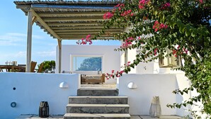 A stone staircase leading to a covered outdoor seating area with a white wall and a wooden pergola. - PAROS HOUSE - Ground Floor of a Villa for 6 persons Private Pool and Sea View (PAROS)