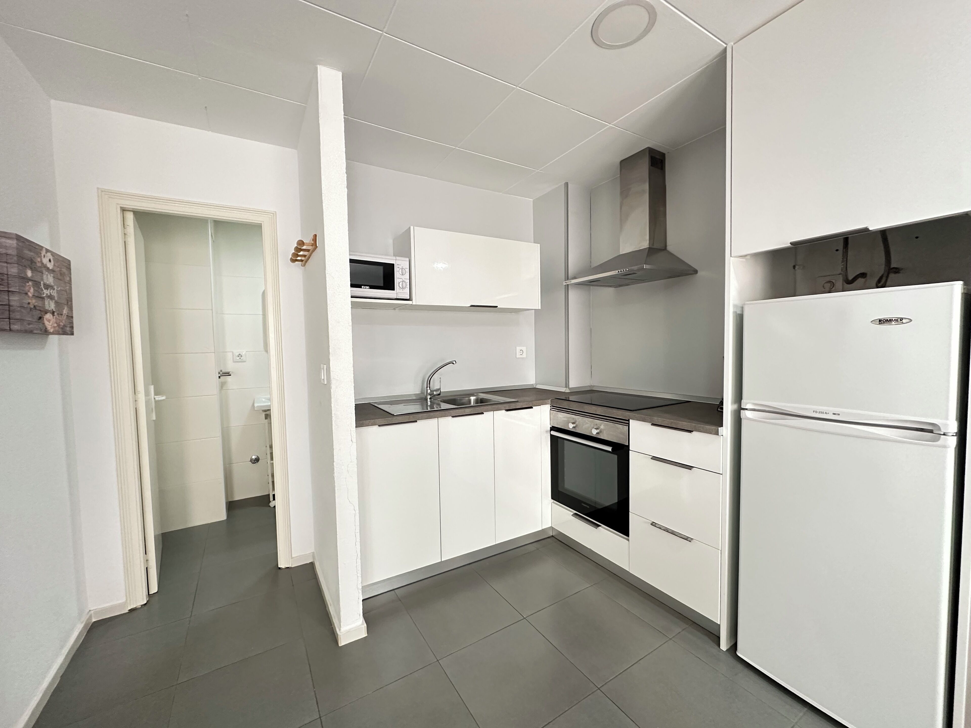 A modern kitchen with white cabinets, a stainless steel sink, a microwave, a stove, and a refrigerator.