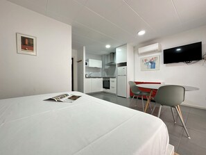 A hotel room with a bed, a small dining table with chairs, a TV mounted on the wall, and a kitchen area visible through an open door. - Agi Arago 151 Apartamento for rent in Roses Girona. (Rosas / Roses)