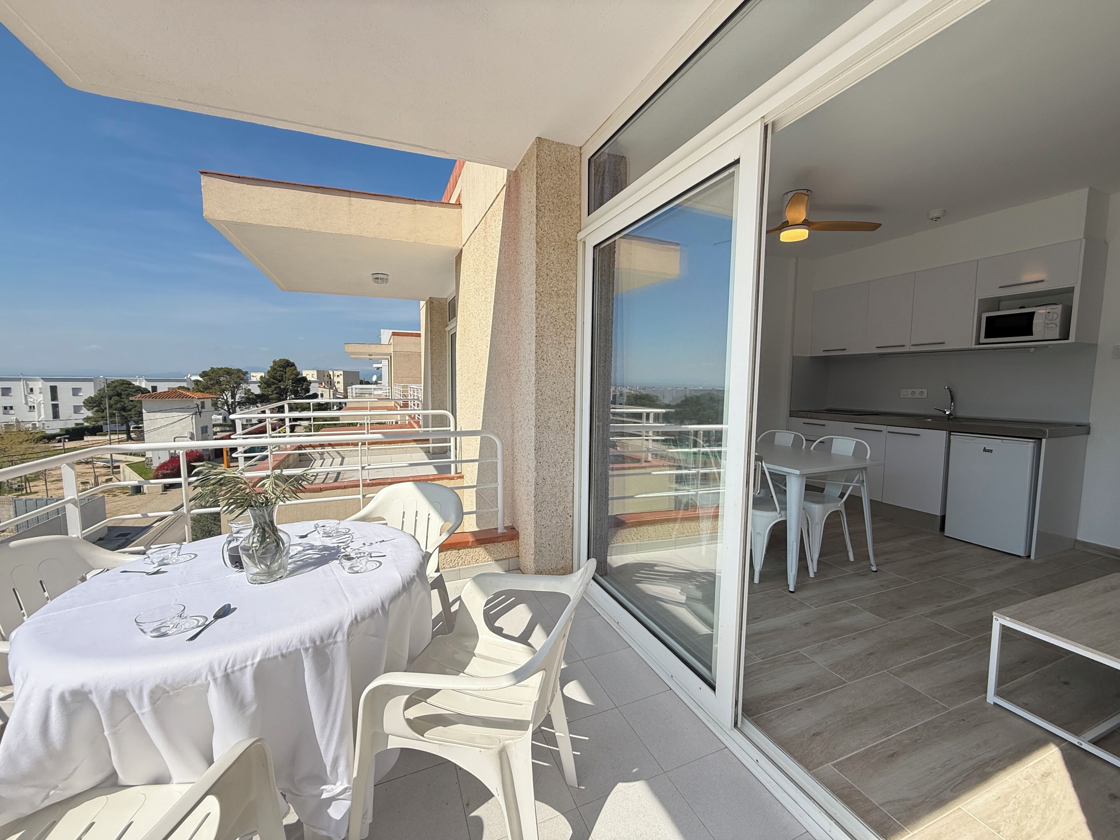 En balkon med et bord og stole, en skydedør til et køkken, og udsigt over bybilledet.