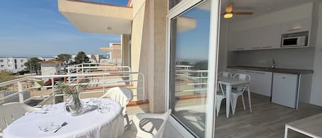 A balcony with a table and chairs, a sliding glass door to a kitchen, and a view of the cityscape.