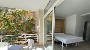 Un balcon avec un lit, une table et des chaises, et une vue sur un arbre et un immeuble.