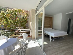 Ein Balkon mit Bett, Tisch und Stühlen, mit Blick auf einen Baum und ein Gebäude.