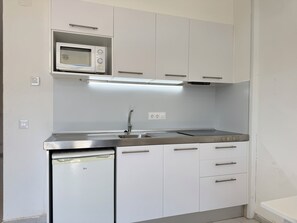 A compact kitchen with a built-in microwave, a stainless steel sink, and white cabinetry.