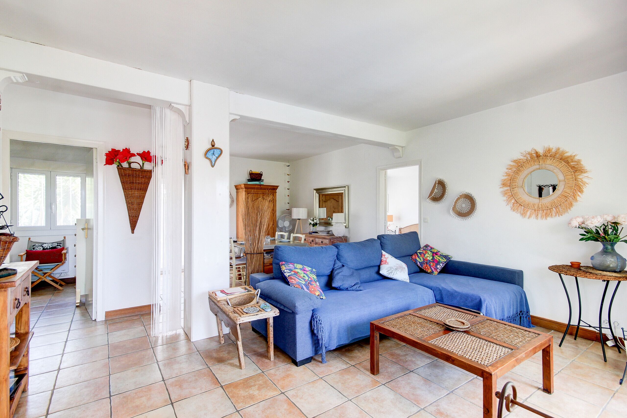 Una sala de estar con un sofá azul, una mesa de centro de madera y una mesita auxiliar de mimbre.