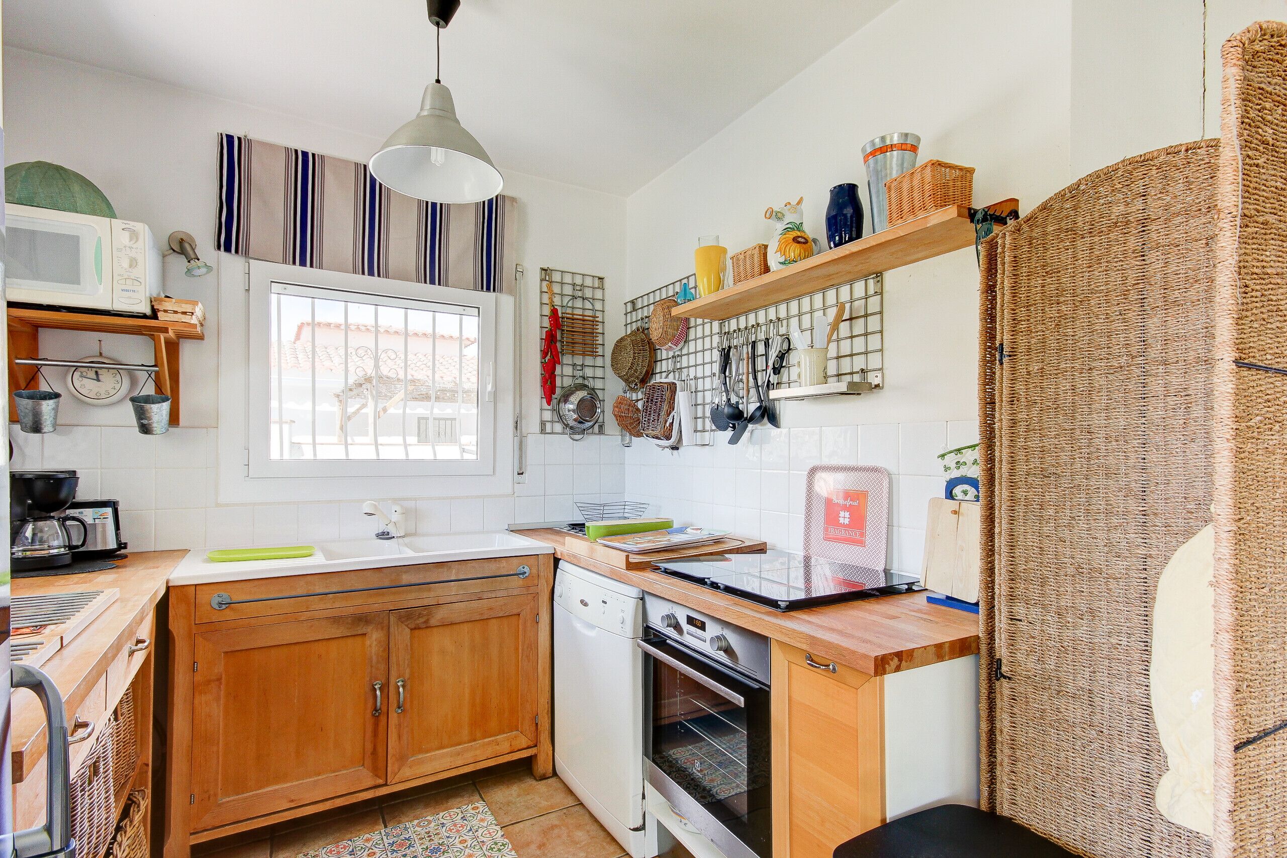 A kitchen with wooden cabinets, a dishwasher, an oven, a window, and various kitchen utensils on shelves.