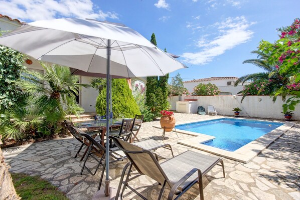 A stone patio with a pool, outdoor furniture, and a large umbrella. - VILLA LA SELVA 26 Roses (Rosas / Roses)