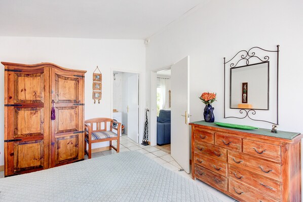 A room with a wooden wardrobe, a wooden dresser, a chair, and a mirror on the wall.