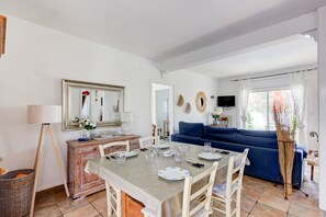 A dining area with a table set for four, a blue sofa, a television, and a wicker basket. - VILLA LA SELVA 26 Roses (Rosas / Roses)